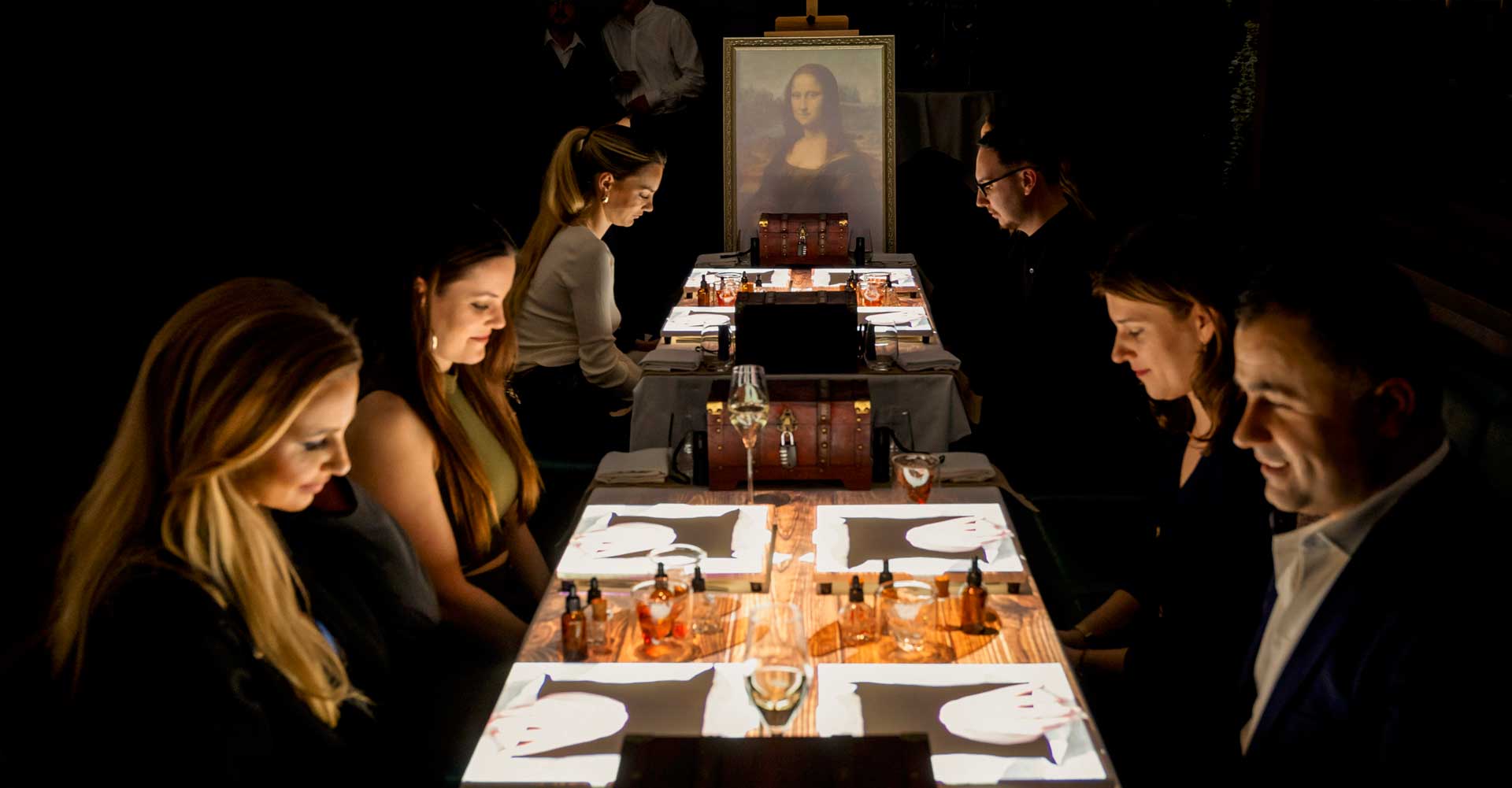 Visitantes cenando bajo la Mona Lisa en una mesa iluminada por proyecciones